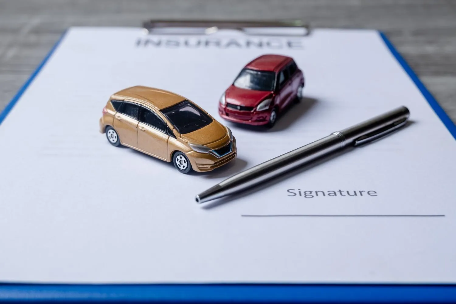 Two model cars and a pen resting on a car insurance form